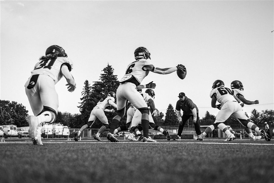 Football players in practice, coach watching from the background — the scene behind the halftime speech