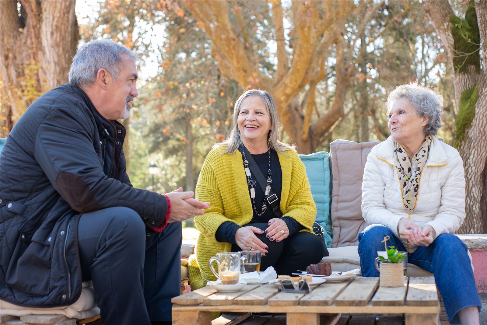 Three older friends talking and laughing over coffee outdoors