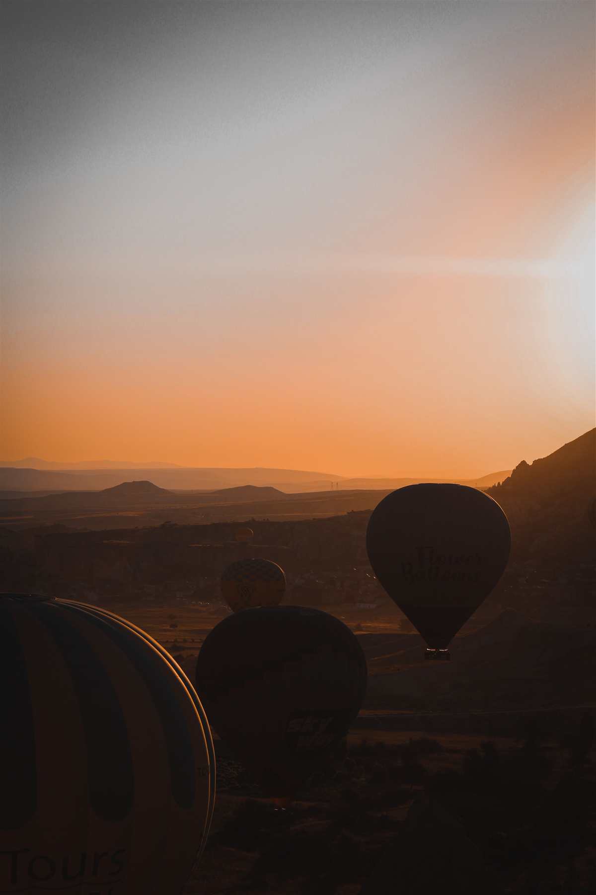 Hot air balloons drifting over Cappadocia at sunrise - golden light, open sky
